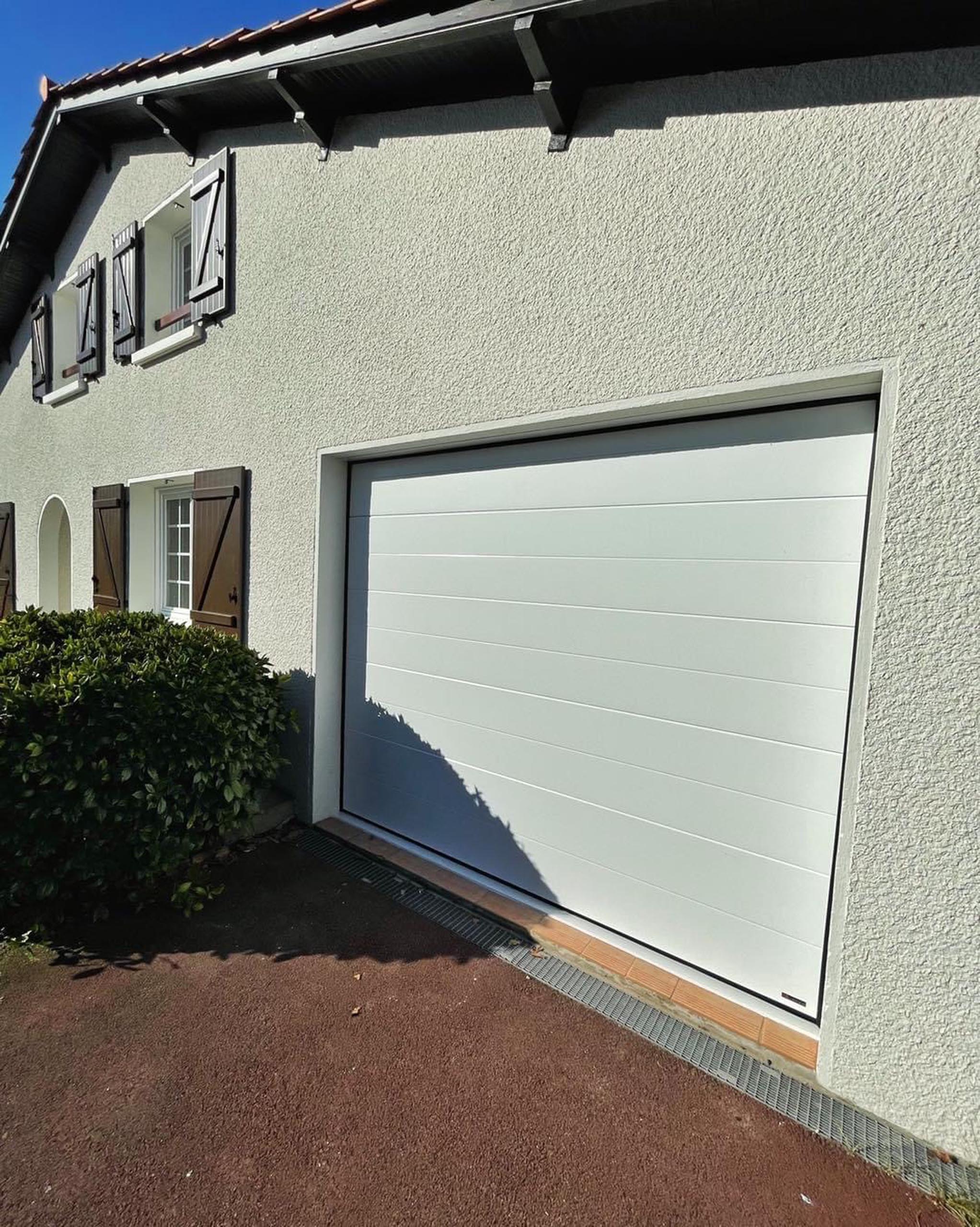 Porte de garage sectionnelle blanche sur une maison crépi avec volets battants