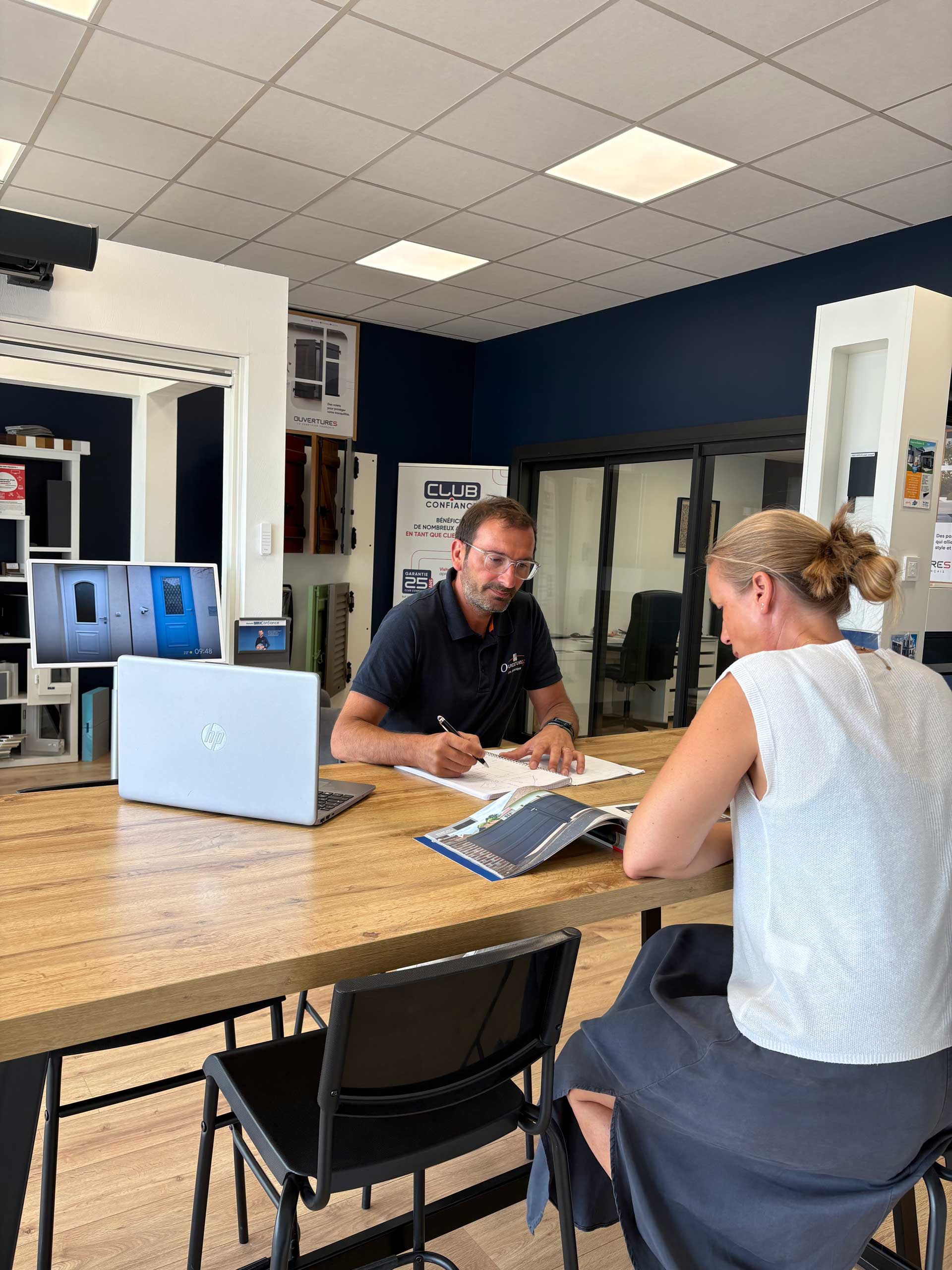 Rendez-vous conseil dans le showroom AM Atlantique à Saint-Jean-d'Illac : un conseiller OuvertureS étudie un projet de menuiserie avec une cliente