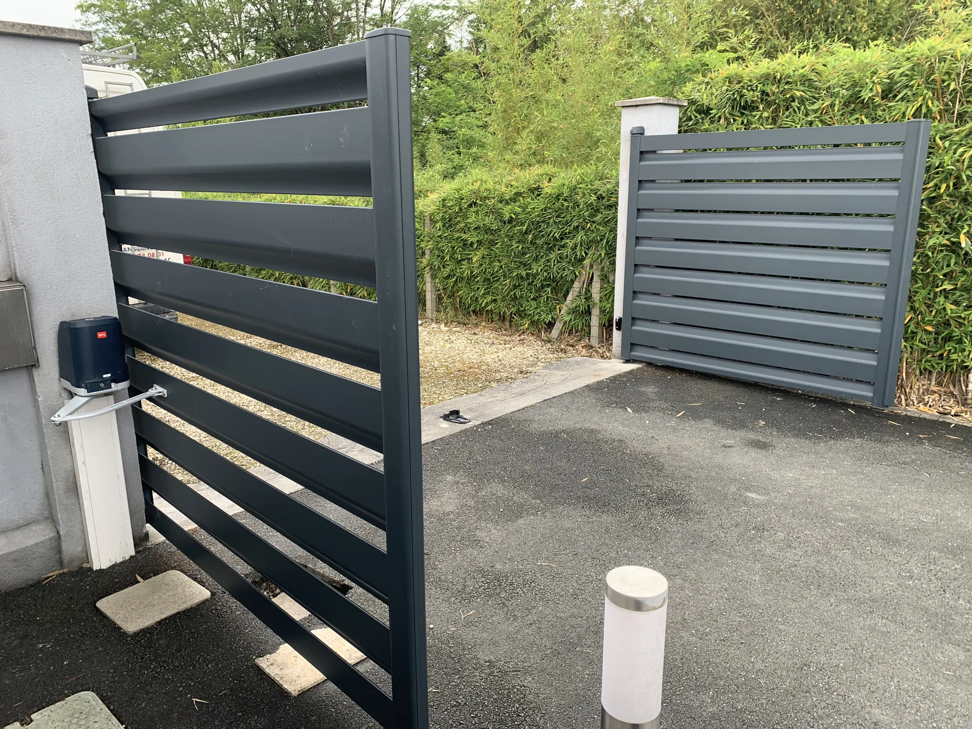 Vantail de portail entrouvert laissant voir la motorisation BFT fixée sur le pilier