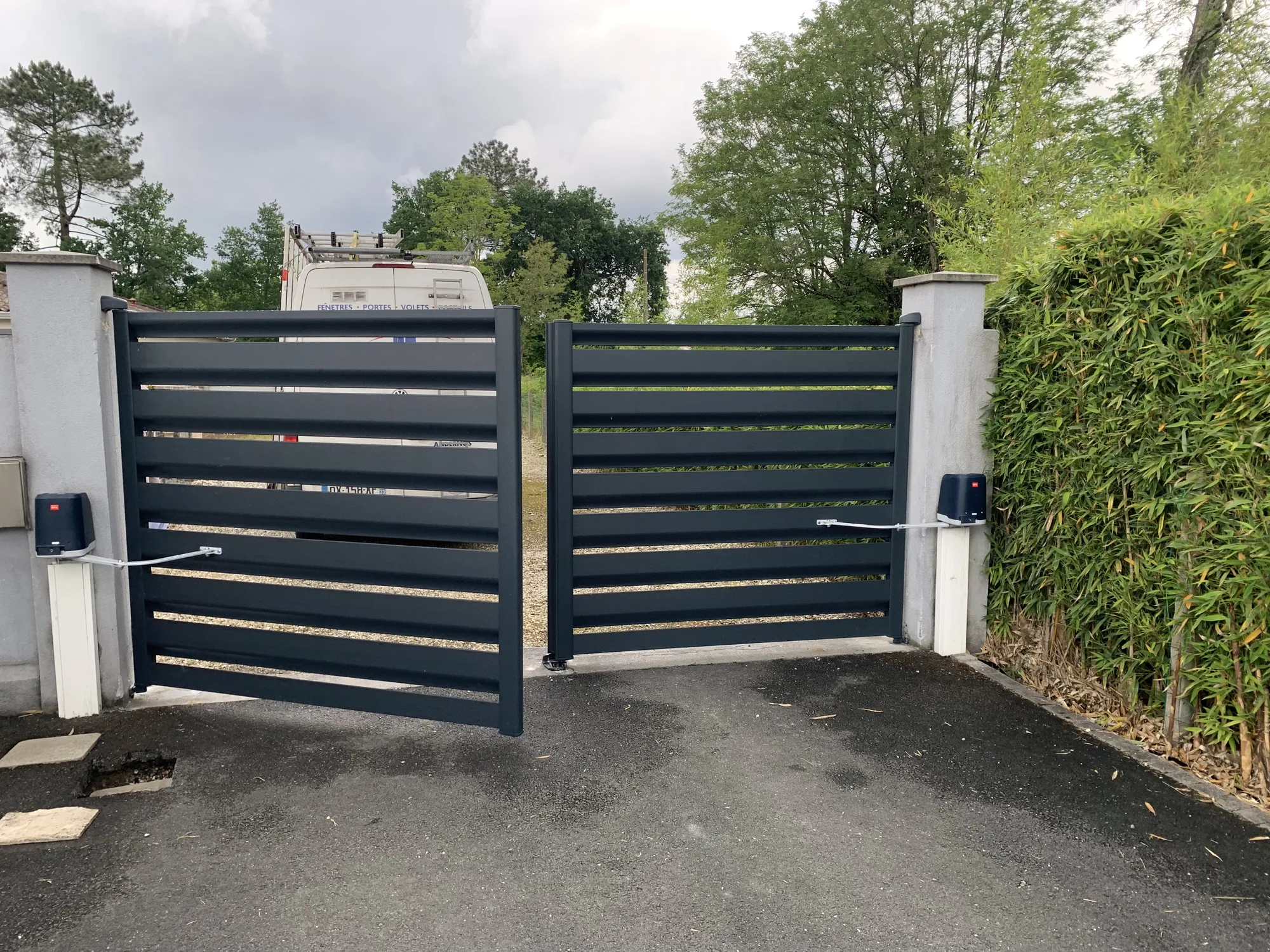Portail battant aluminium en cours d'ouverture motorisée, vue depuis l'allée de la propriété