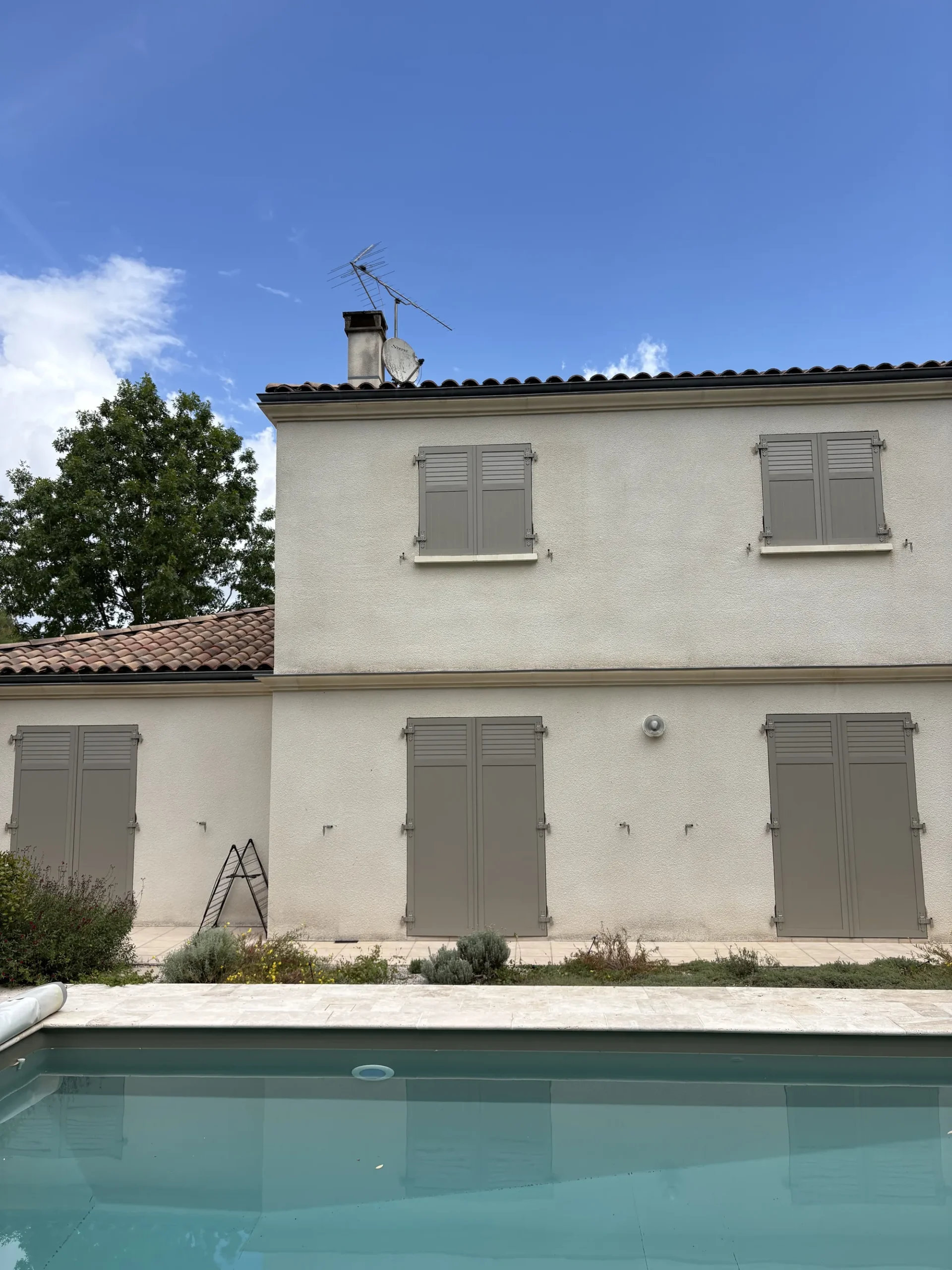 Façade arrière d'une maison à Gradignan équipée de volets battants aluminium gris sable, vue depuis la piscine