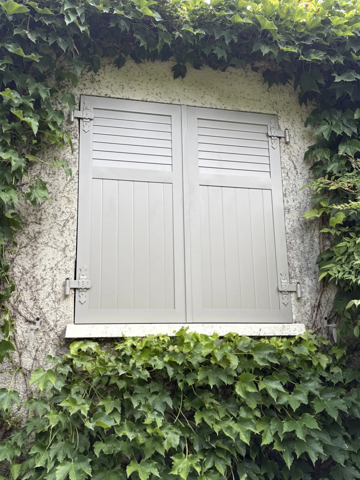 Volet battant aluminium ouvert laissant apparaître une fenêtre PVC à petits carreaux