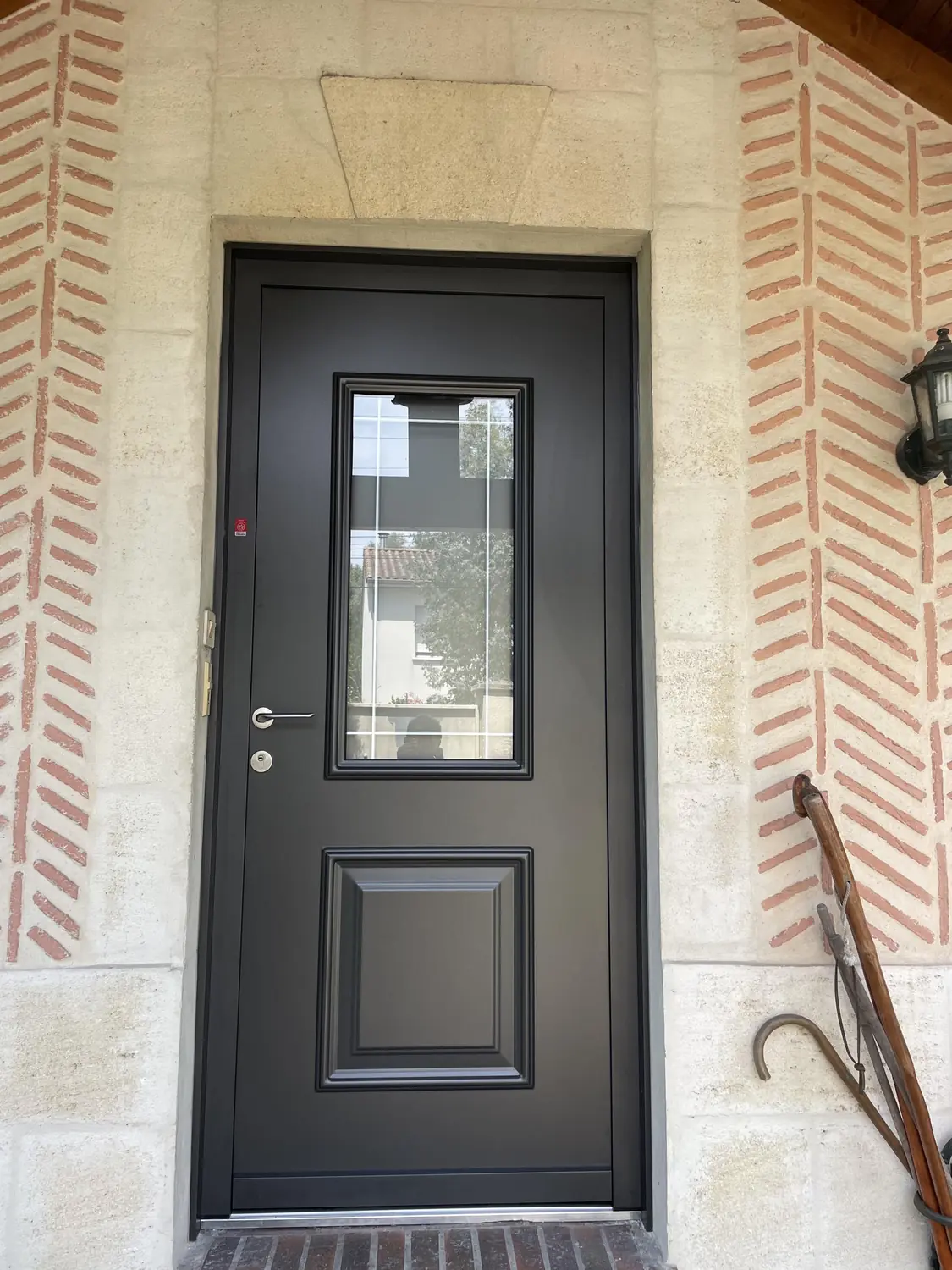 Porte d'entrée en aluminium anthracite semi-vitrée sur une façade en brique