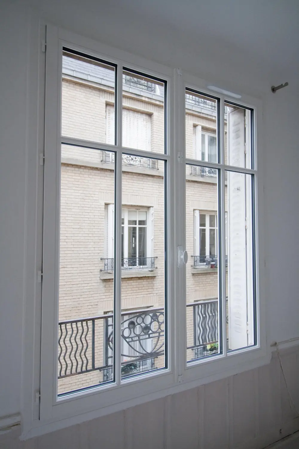 Fenêtre bois laquée blanche à petits bois vue de l'intérieur sur un immeuble ancien