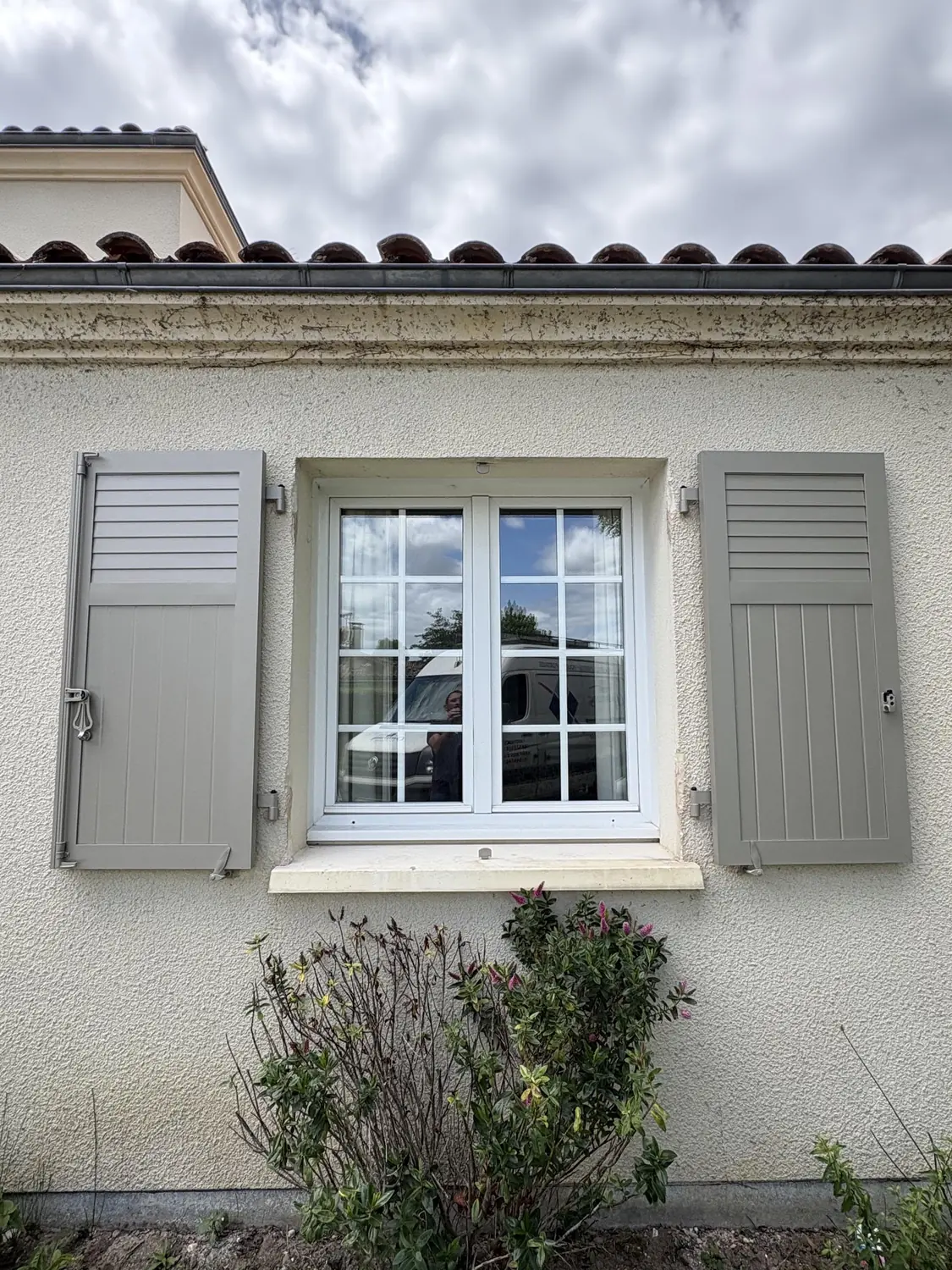 Volets battants à persienne gris clair sur une fenêtre à appui de pierre