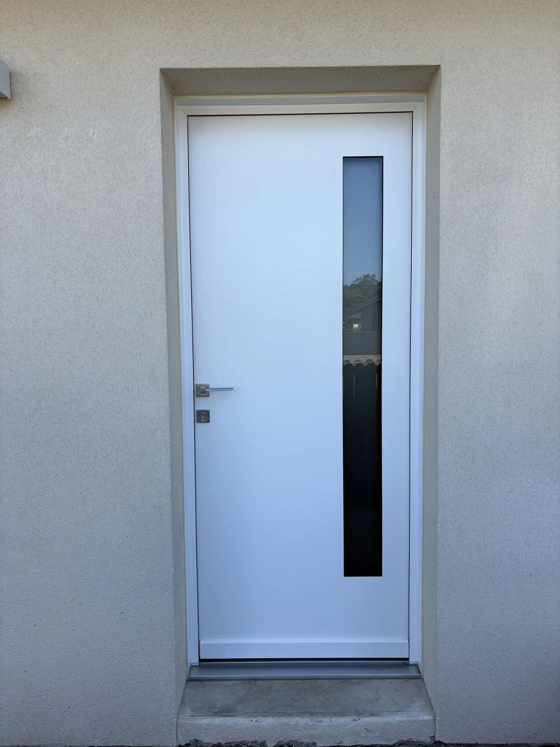 Porte d’entrée blanche dans son tableau maçonné et son seuil béton