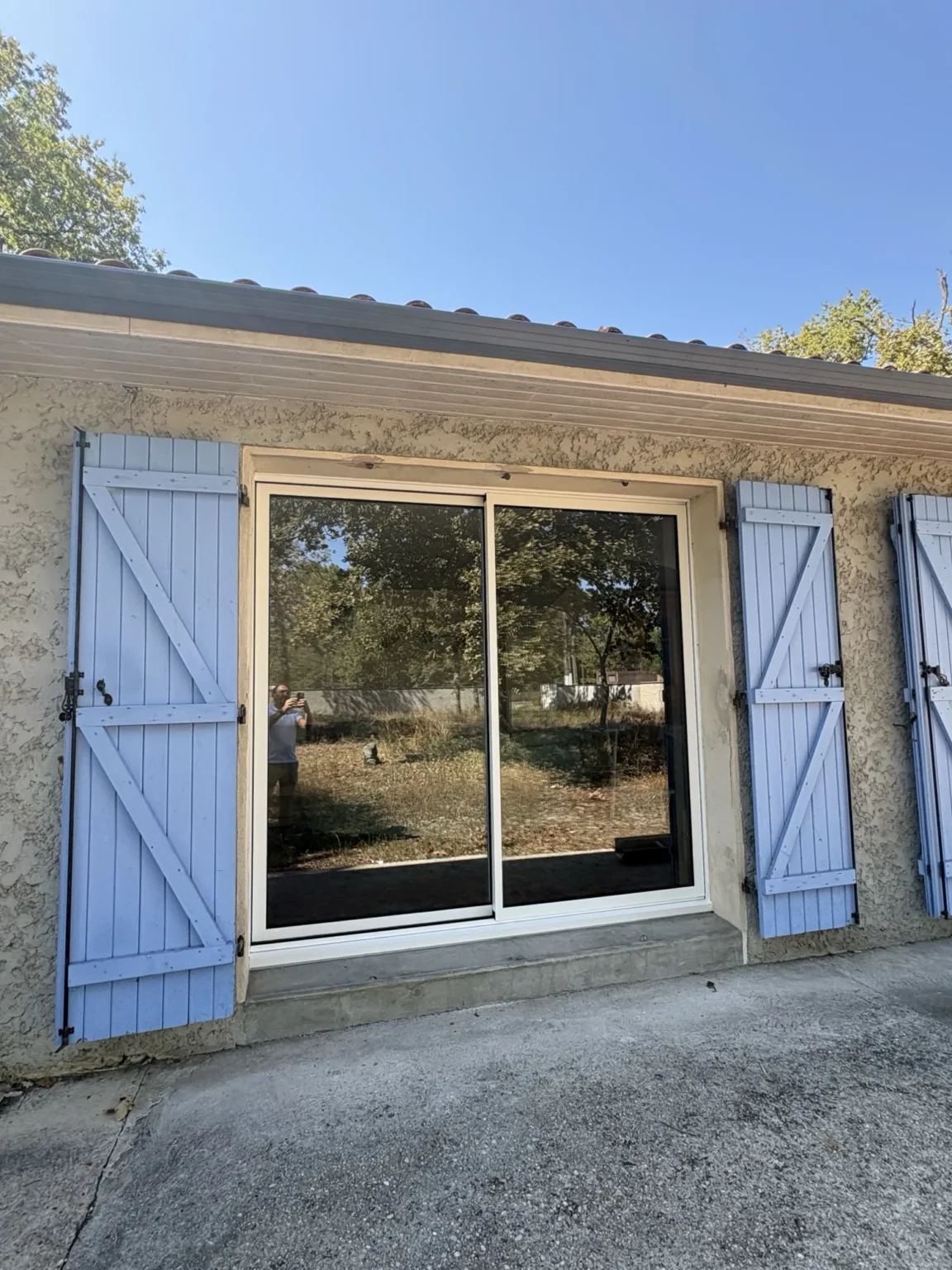 Baie coulissante aluminium blanche à deux vantaux posée en dépose totale, encadrée de volets battants bois