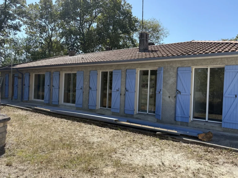 Façade côté jardin d’une maison de plain-pied au Pian-Médoc après le remplacement des menuiseries aluminium, volets bois bleus ouverts
