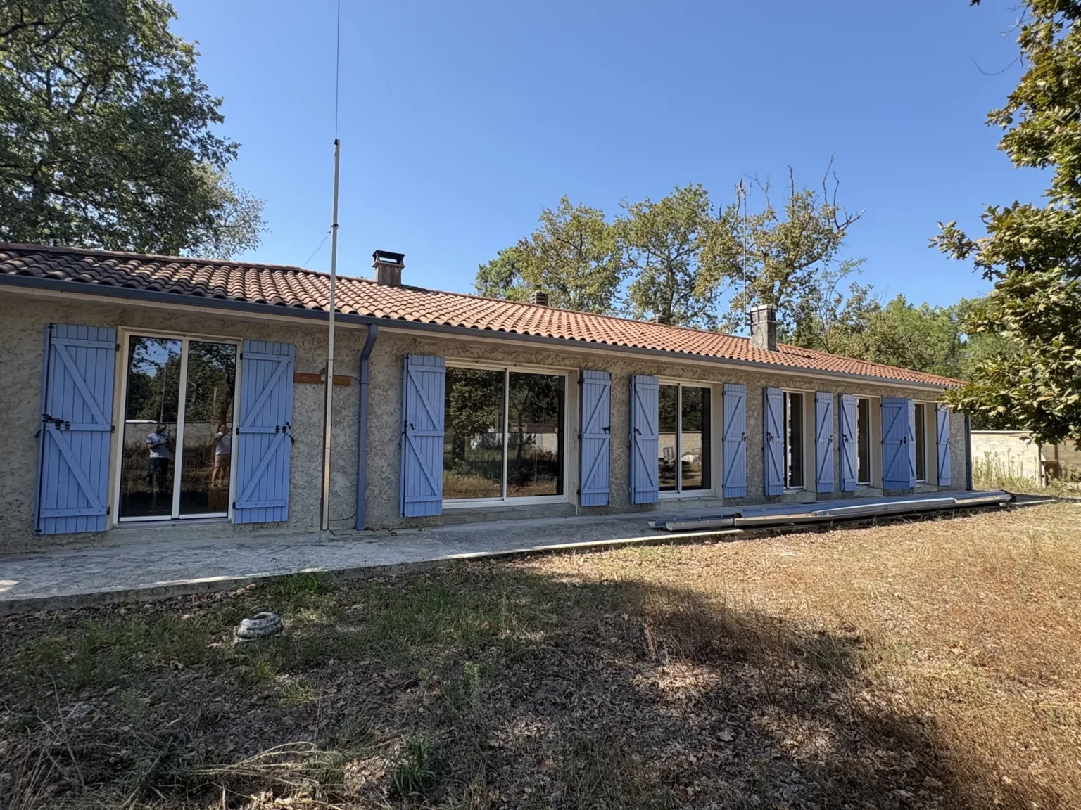 Maison de plain-pied crépie et son alignement de portes-fenêtres aluminium blanches, sur un terrain arboré