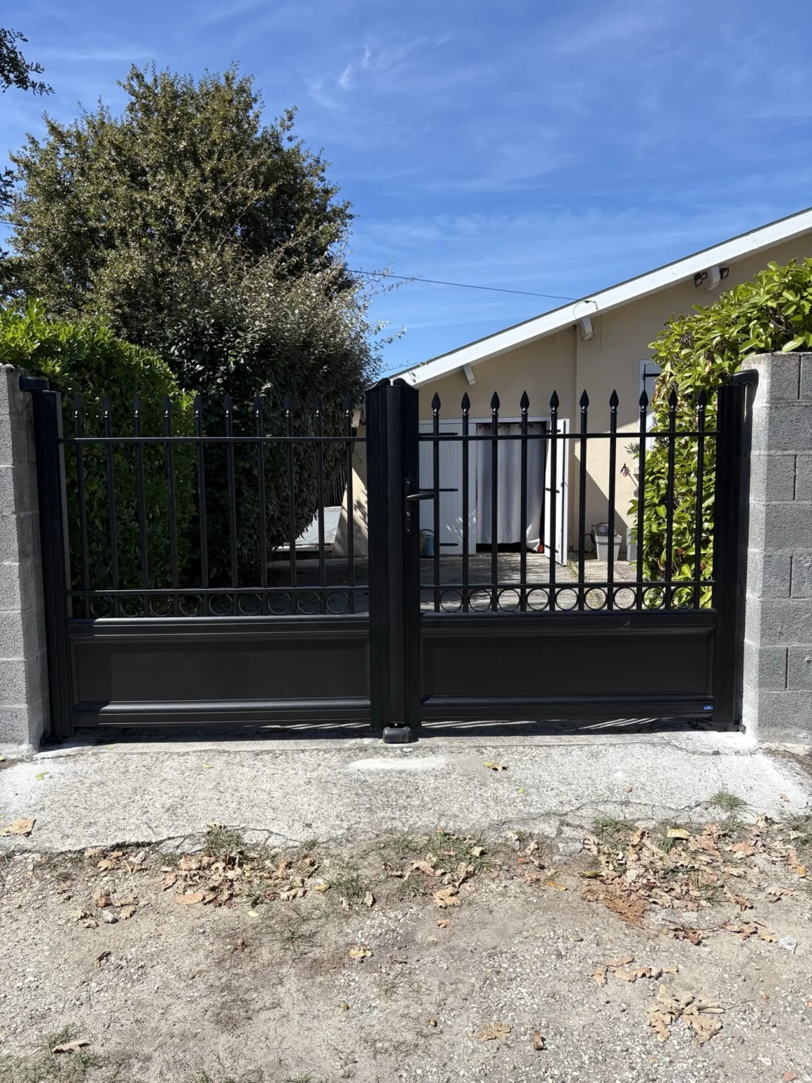 Portail aluminium fermé devant l’allée d’une maison de plain-pied, haies de part et d’autre