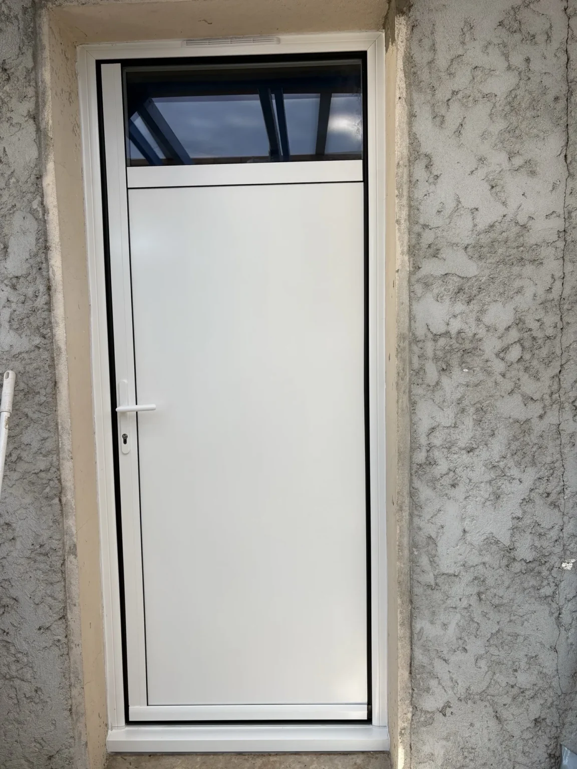 Porte de service aluminium blanche à panneau plein et imposte vitrée, posée dans un mur crépi