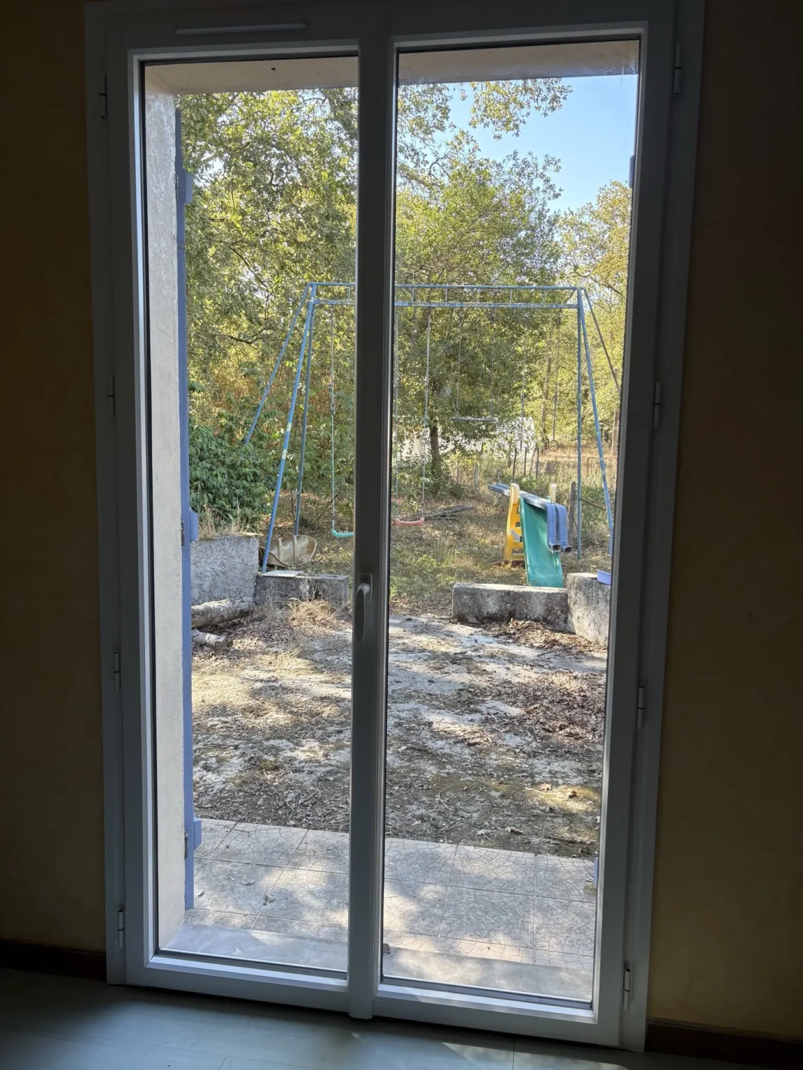 Vue intérieure d’une porte-fenêtre aluminium ouvrant sur le jardin, entrée d’air intégrée en traverse haute