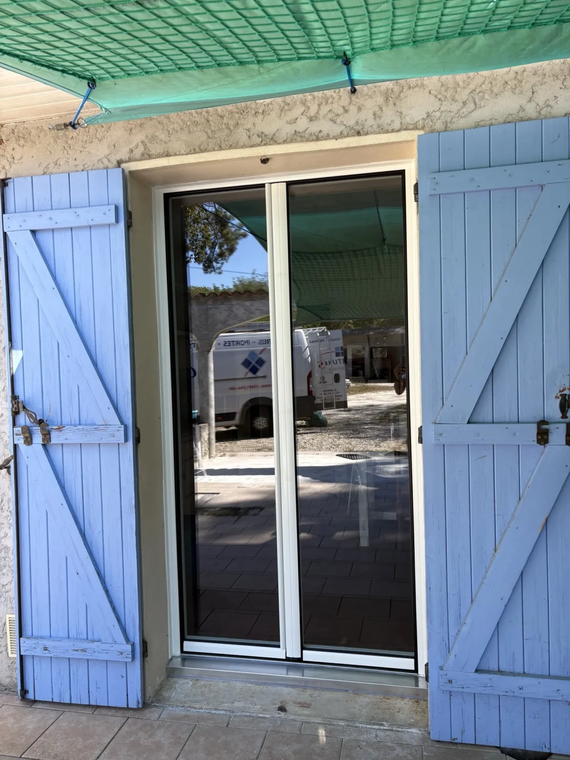 Porte-fenêtre aluminium donnant sur une terrasse carrelée, côté cour de la maison